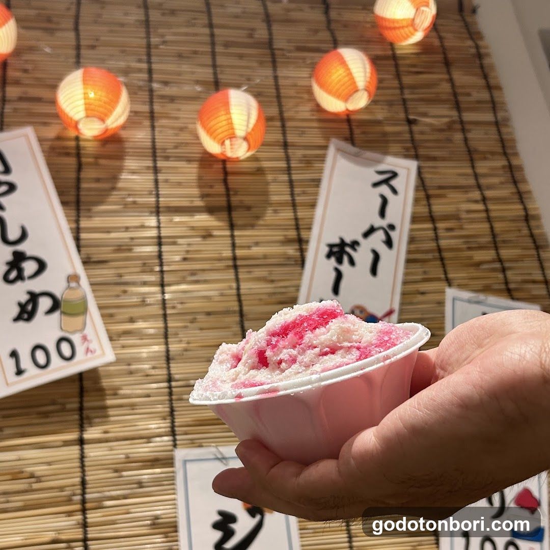 Hand holding pink shaved ice with lanterns in background
