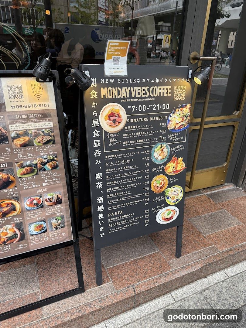 A street-level view of a cafe entrance featuring two prominent menu boards on the sidewalk. The main board advertises 'NEW STYLE Cafe & Italian Bar' with operating hours and signature dishes like pasta and steak. A secondary board lists breakfast items, including toast sets and pancakes. The shop has glass doors with gold handles and is situated in an urban area.