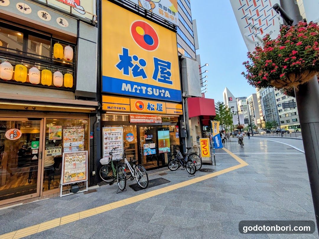 A street-level view of a Matsuya restaurant storefront with visible signage, lanterns, and bicycles parked outside.