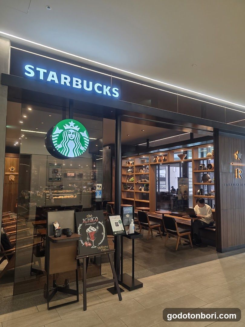 A Starbucks storefront with illuminated signage and a visible entrance. Inside, wooden shelves display various items, and customers are seated at tables.