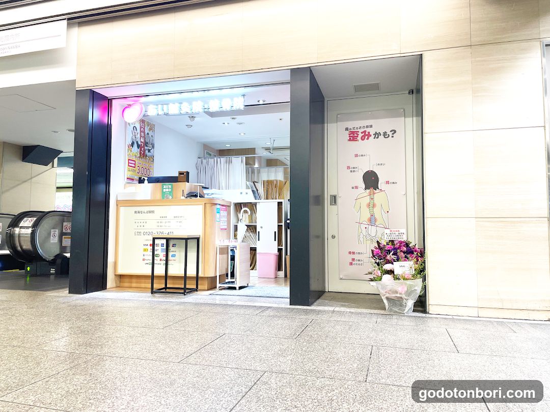 A brightly lit storefront entrance with a reception desk, posters advertising treatments like 'Shinrin-yoku' (forest bathing), and a floral arrangement outside.