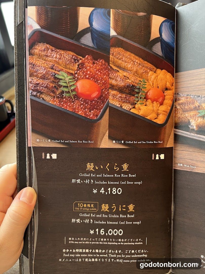 A close-up of a Japanese restaurant menu page held by a hand, featuring two eel rice bowl dishes with prices and descriptions in Japanese and English.