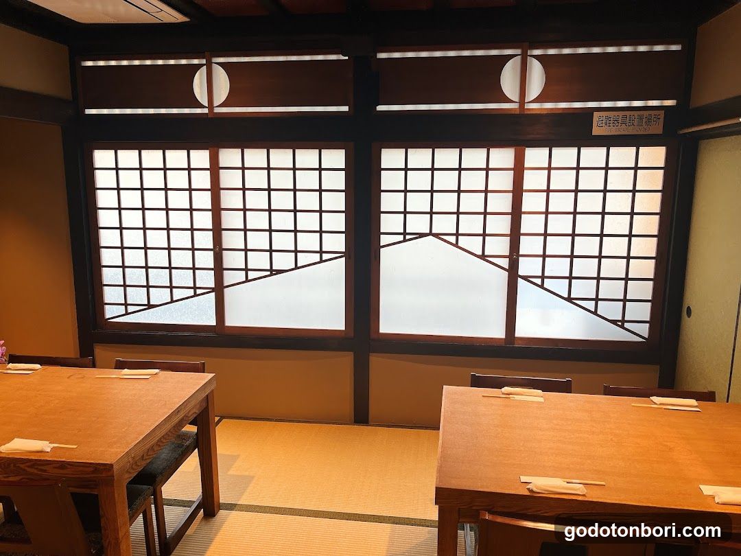 Interior view of a traditional Japanese dining space featuring tatami flooring, wooden tables with chopsticks and napkins, and shoji screens depicting mountain landscapes. A small sign on the wall reads '乾物類設置場所' (Dried Goods Storage Area). No menu or exterior signage is visible.