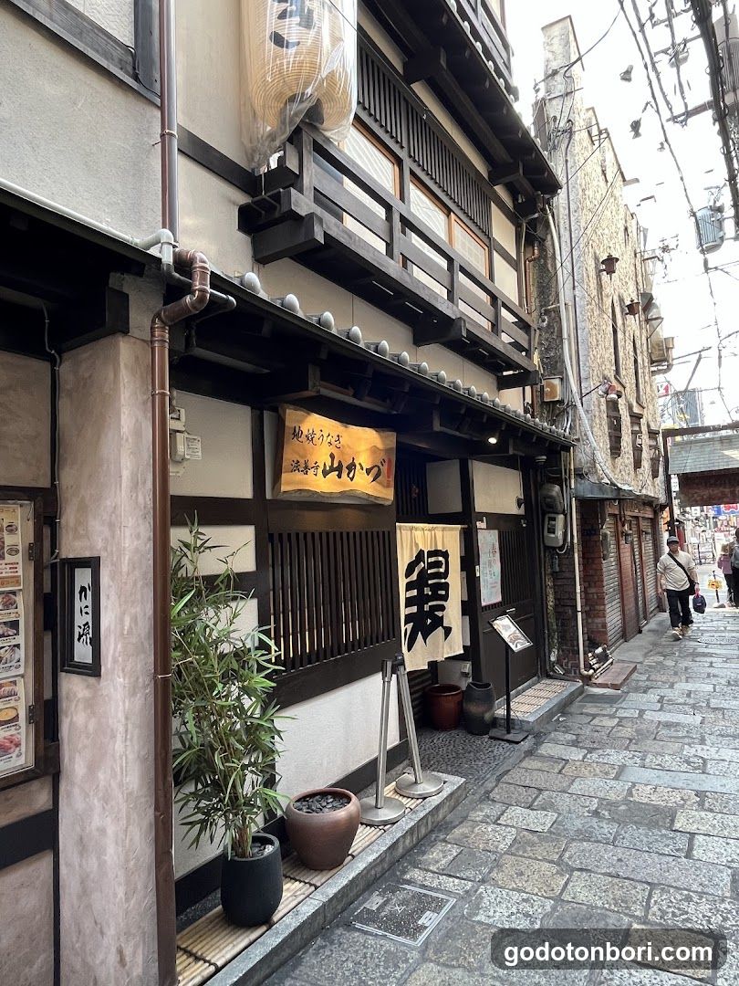 A traditional Japanese shop with wooden exterior, bamboo planters, and signage featuring Japanese characters. The building has a classic architectural style with visible pipes and lanterns.