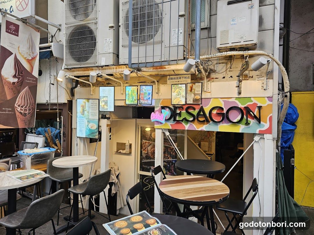 A small shop with a colorful 'DESAGON' sign on the facade, featuring outdoor seating and digital menu boards.