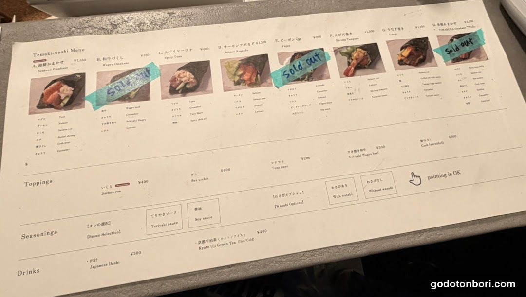 A printed sushi menu featuring tenaki (rolled sushi) options with prices in yen, some marked as sold out.