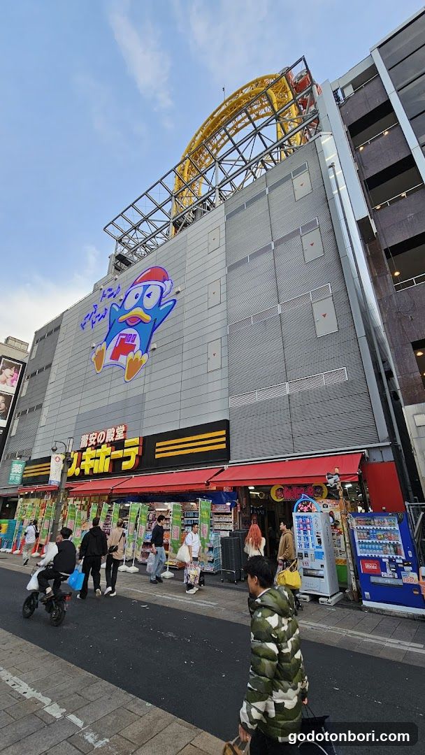 A multi-story commercial building with a large cartoon character logo on the facade, featuring red awnings over storefronts and visible signage in Japanese characters.
