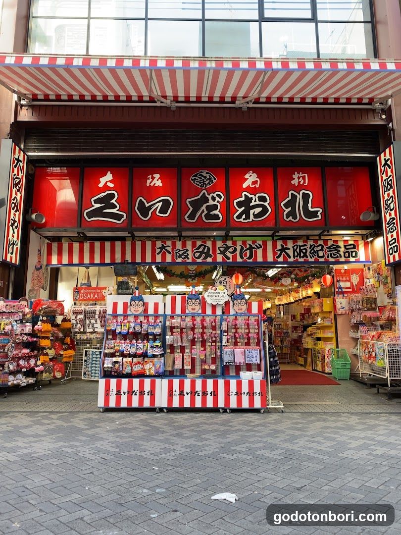 A shop front with a red and white striped awning, featuring large Japanese characters on the facade. The entrance is adorned with colorful displays of merchandise, including packaged goods and souvenirs.