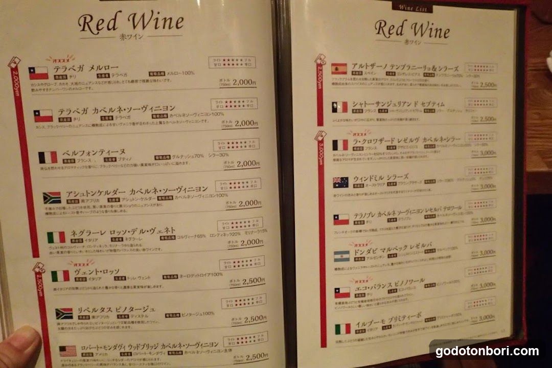 A close-up of a wine menu featuring red wines with Japanese and English descriptions, prices in yen, and flags indicating origin countries.