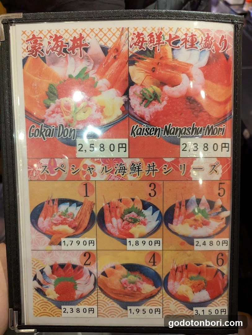 A framed menu board displaying various seafood rice bowls (donburi) with prices in yen. The top section features two large items: 'Gokai Don' at ¥2,580 and 'Kaisen Nanashu Mori' at ¥2,380. Below is a series of six smaller options labeled 1 through 6, ranging from ¥1,790 to ¥3,150. Each item includes an image of the dish and its price.