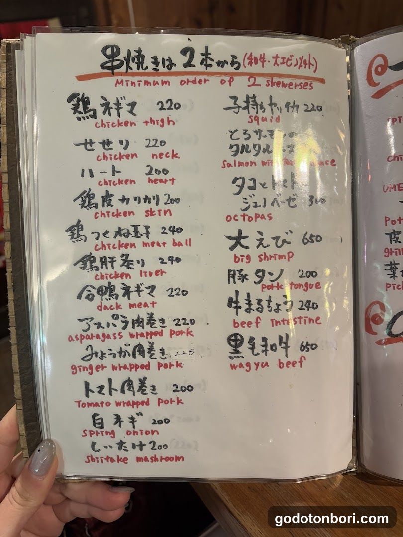 A close-up of a handwritten yakitori menu in Japanese and English, listing skewered meats with prices.