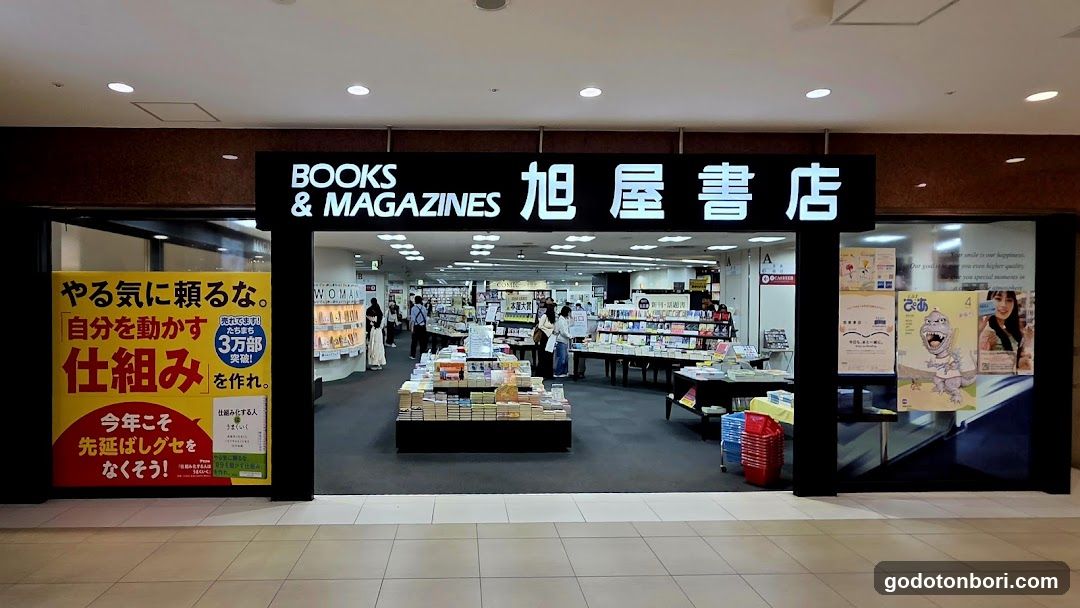 The image shows the entrance of a bookstore with signage reading 'BOOKS & MAGAZINES' and Japanese characters. Inside, shelves are stocked with books and magazines. A poster on the left promotes self-motivation in Japanese.