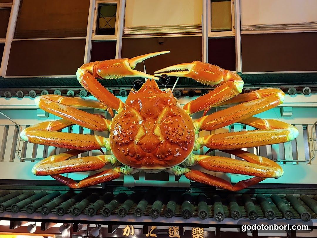 A large, illuminated crab sculpture is mounted above the entrance of a building. The crab is orange and yellow with detailed claws and legs. Below the crab, there are Chinese characters on a sign.