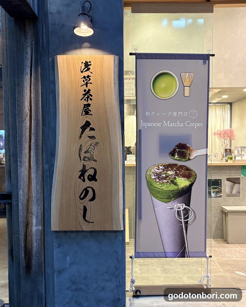 A shop entrance featuring a wooden sign with Japanese characters and a vertical banner advertising 'Japanese Matcha Crepes' with images of matcha crepe cones.