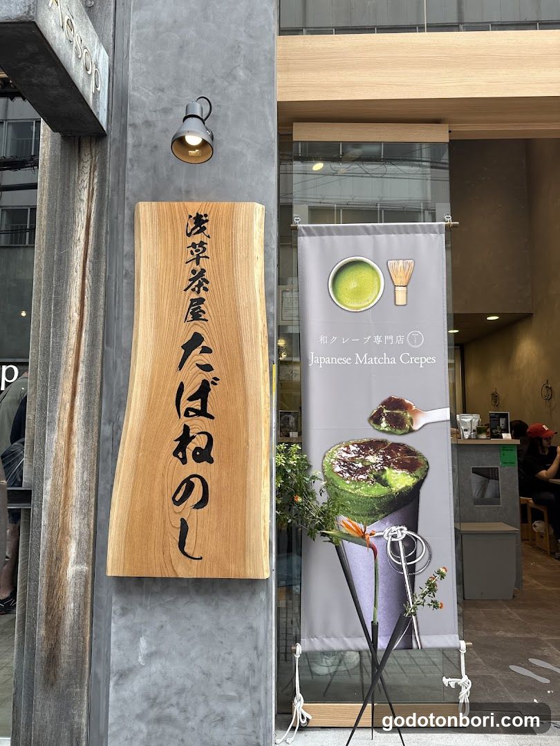A shop front featuring a wooden sign with Japanese characters, a banner advertising matcha crepes, and a glimpse into the interior.