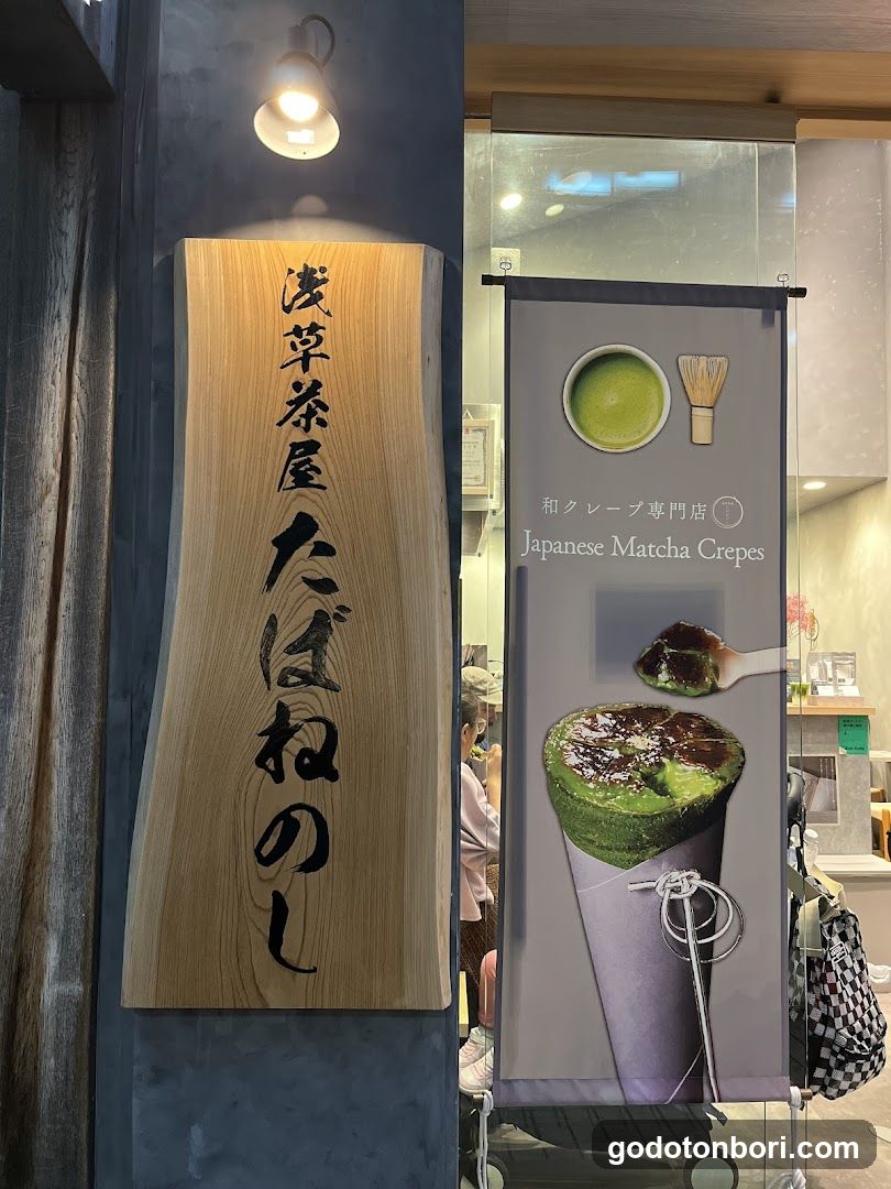 A shop front featuring a wooden sign with Japanese characters and a vertical banner advertising 'Japanese Matcha Crepes' with images of matcha-flavored crepe products.